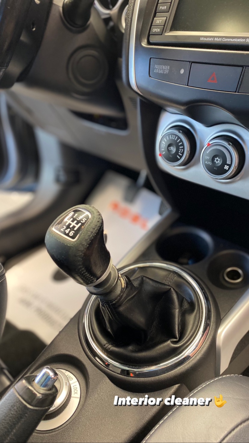 Wnętrze samochodu z dźwignią zmiany biegów manualnej skrzyni biegów, widoczne elementy deski rozdzielczej i panel klimatyzacji.