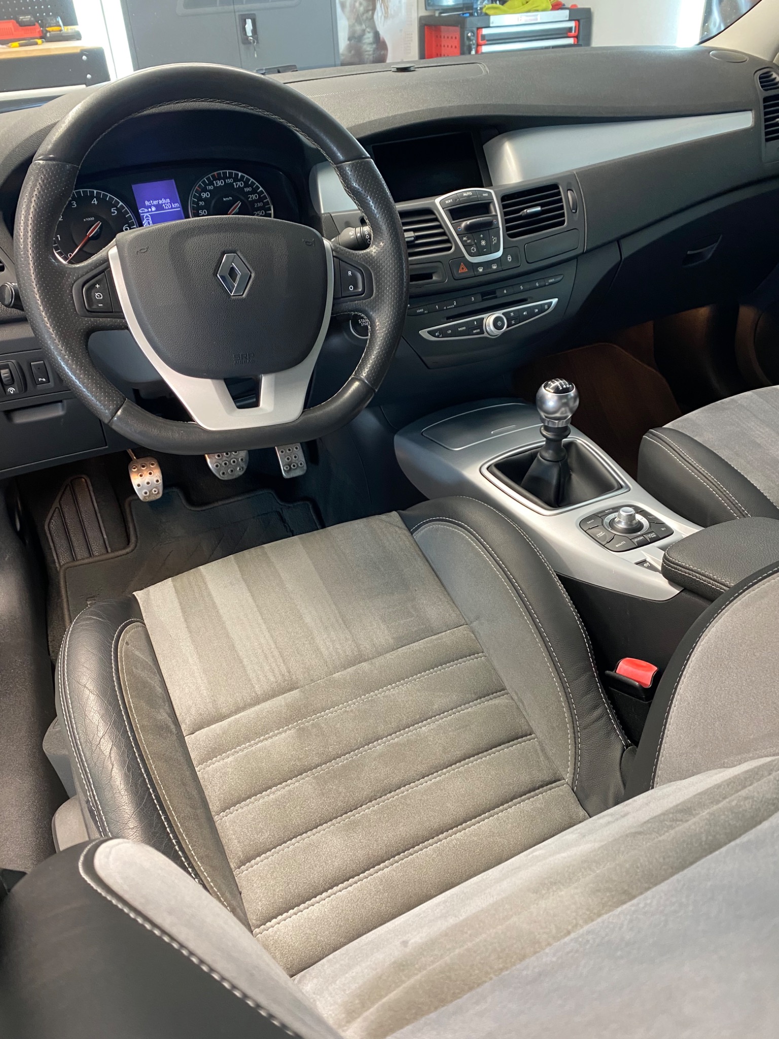 Wnętrze samochodu Renault Laguna z widocznym fotelem kierowcy z szarej alcantary z ciemniejszymi skórzanymi bokami, kierownicą z logo Renault oraz deską rozdzielczą po zabiegu czyszczenia, widoczne...