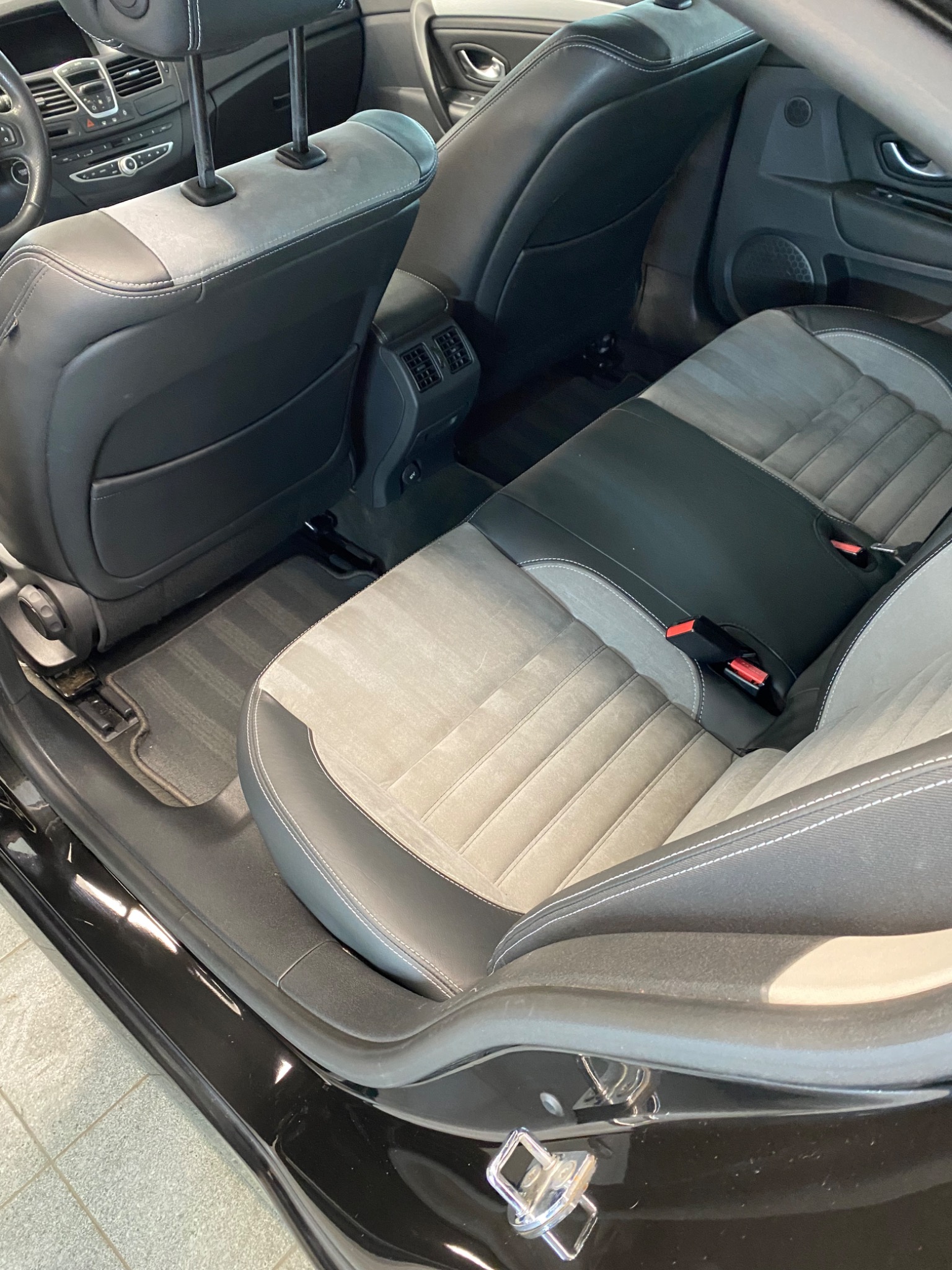 Wnętrze czarnego samochodu: tylna kanapa z jasną, prążkowaną tapicerką i czarnymi elementami skórzanymi, widoczne pasy bezpieczeństwa i zagłówki.