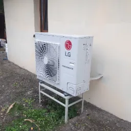 Biała jednostka zewnętrzna pompy ciepła LG Therma V, zamontowana na metalowym stelażu przy jasnej ścianie budynku z widocznym oknem.