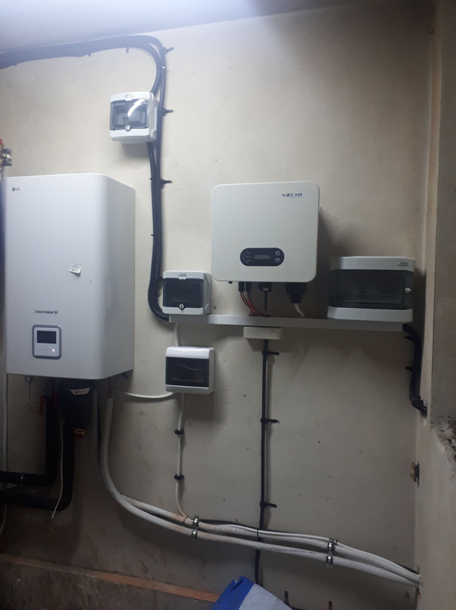 Instalacja wewnętrzna z pompą ciepła LG Therma V i inwerterem SOFAR, z widocznymi przewodami i skrzynkami zabezpieczeń na ścianie w pomieszczeniu technicznym.