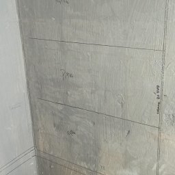 Wykończenia Przemysław Robert - Przygotowana do położenia płytek ściana w rogu łazienki z zaznaczonym poziomem, widoczne kliny dystansowe i data zdjęcia.