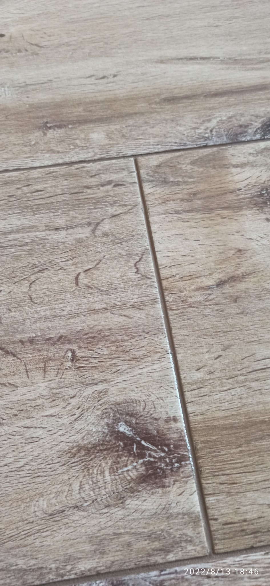 Ułożona podłoga z paneli imitujących drewno w ciepłych odcieniach brązu, widoczne łączenia między panelami.