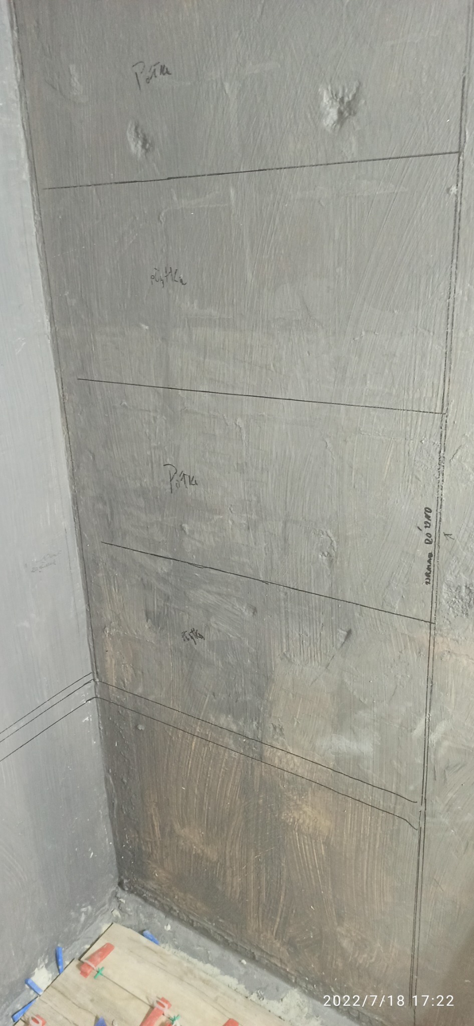 Przygotowana do położenia płytek ściana w rogu łazienki z zaznaczonym poziomem, widoczne kliny dystansowe i data zdjęcia.