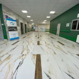 Wnętrze wyczyszczonego korytarza szpitalnego w Gostyninie, z marmurową posadzką i zielonymi ścianami, po zakończonych pracach remontowych. Na ścianie widoczne tablice informacyjne i plan budynku.