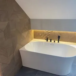 Nowoczesna łazienka z wolnostojącą białą wanną, geometryczną okładziną ścienną z podświetleniem LED i czarną armaturą.