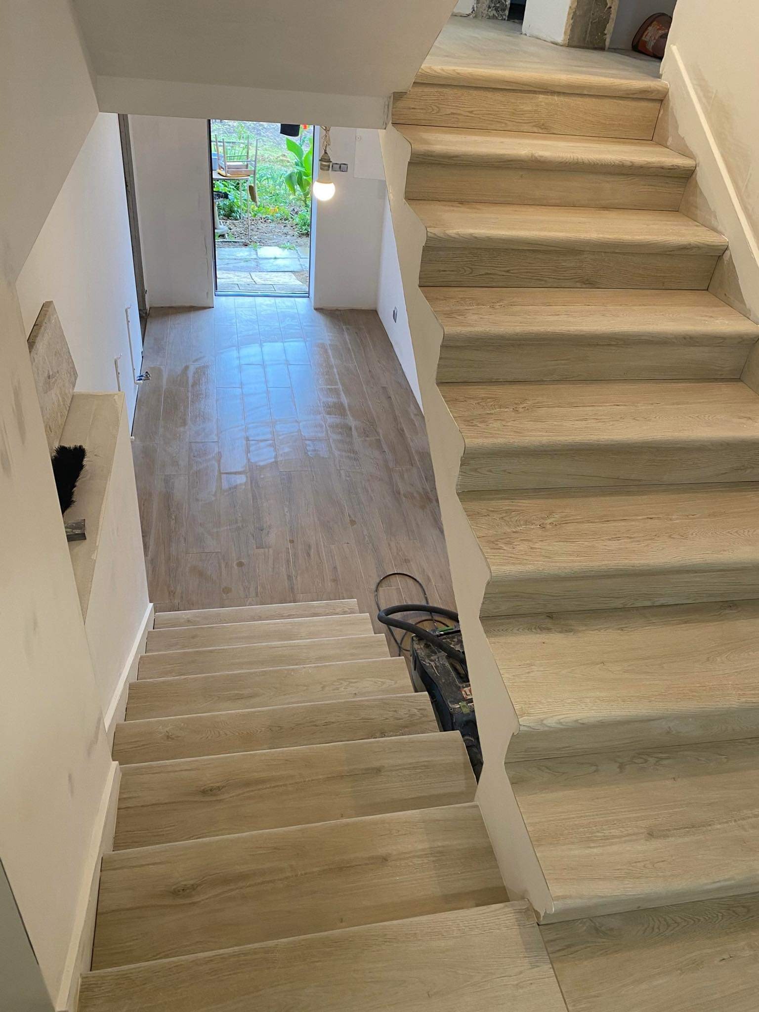 Schody wyłożone panelami drewnopodobnymi w trakcie montażu, widok z góry, z widocznym odkurzaczem budowlanym i świeżo położoną podłogą w korytarzu.