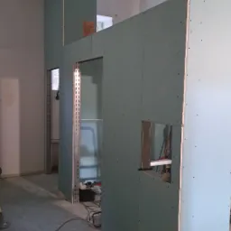 Montaż ścian działowych z płyt karton-gips na metalowym stelażu, widoczne narzędzia i kable na podłodze, surowy stan wykończenia wnętrza biura.