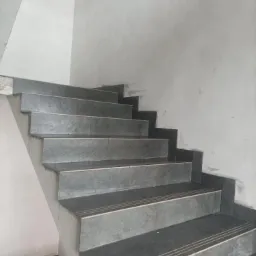 Wykończone schody z szarymi płytkami imitującymi kamień, z widocznymi trzema ciemnymi paskami na każdym stopniu, ściany surowe, przygotowane do malowania.
