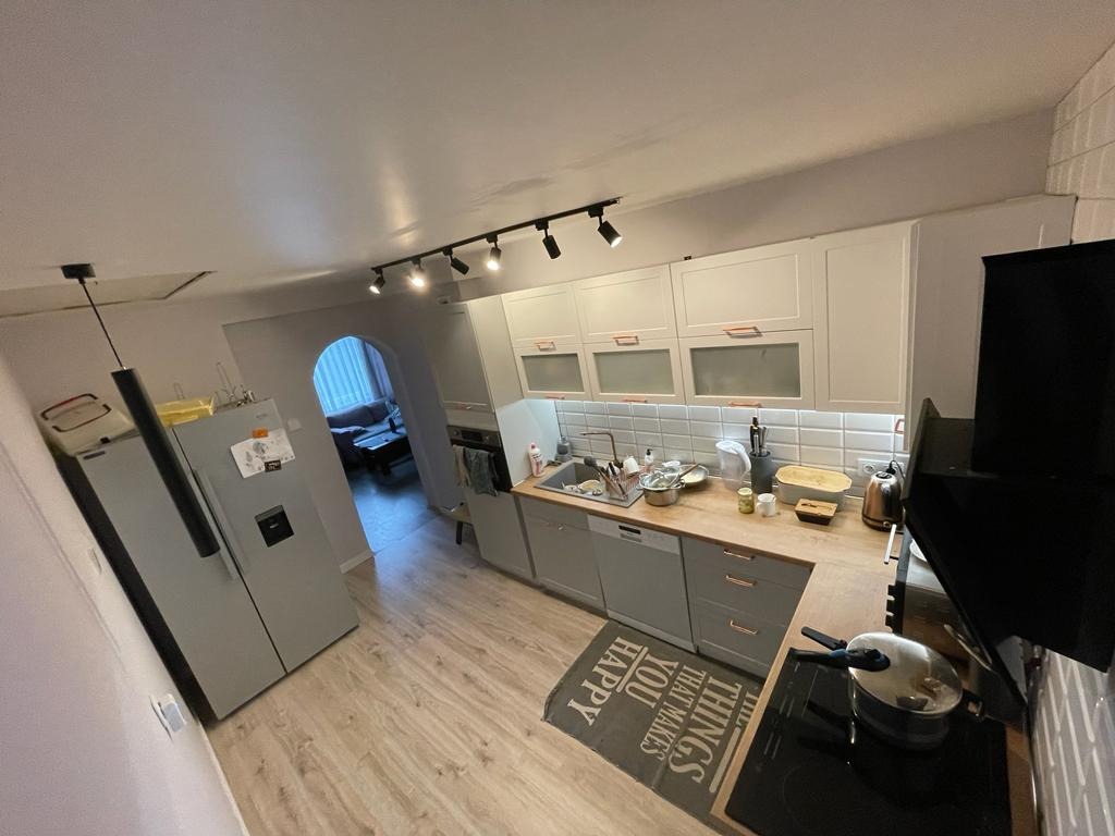 Szare szafki kuchenne z drewnianym blatem i białymi płytkami na ścianie, widok na salon przez łukowate przejście