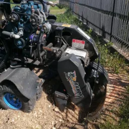 Frezarka do pni Bandit z silnikiem Kubota, widoczne świeże wióry po frezowaniu pnia, w tle szary płot i słup wysokiego napięcia.