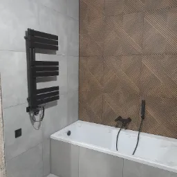 Wykończona łazienka w Ożarowie Mazowieckim z wanną w obudowie z szarych płytek, czarnym grzejnikiem drabinkowym na ścianie i dekoracyjną ścianą z płytek o geometrycznym wzorze w odcieniach brązu.
