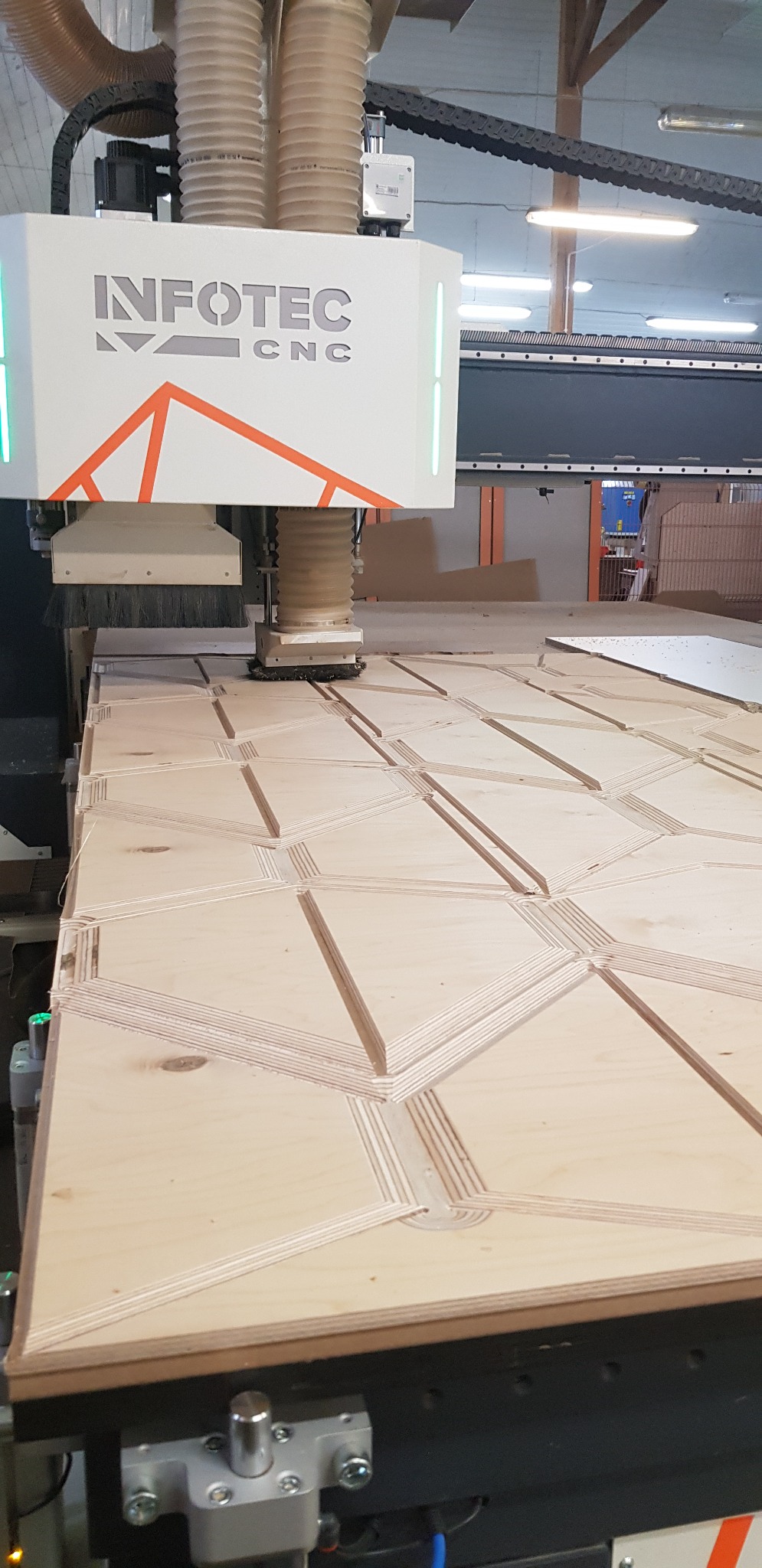 Frezarka CNC Infotec wycina wzór geometryczny z płyty drewnianej, widoczne wióry i detale frezowania.