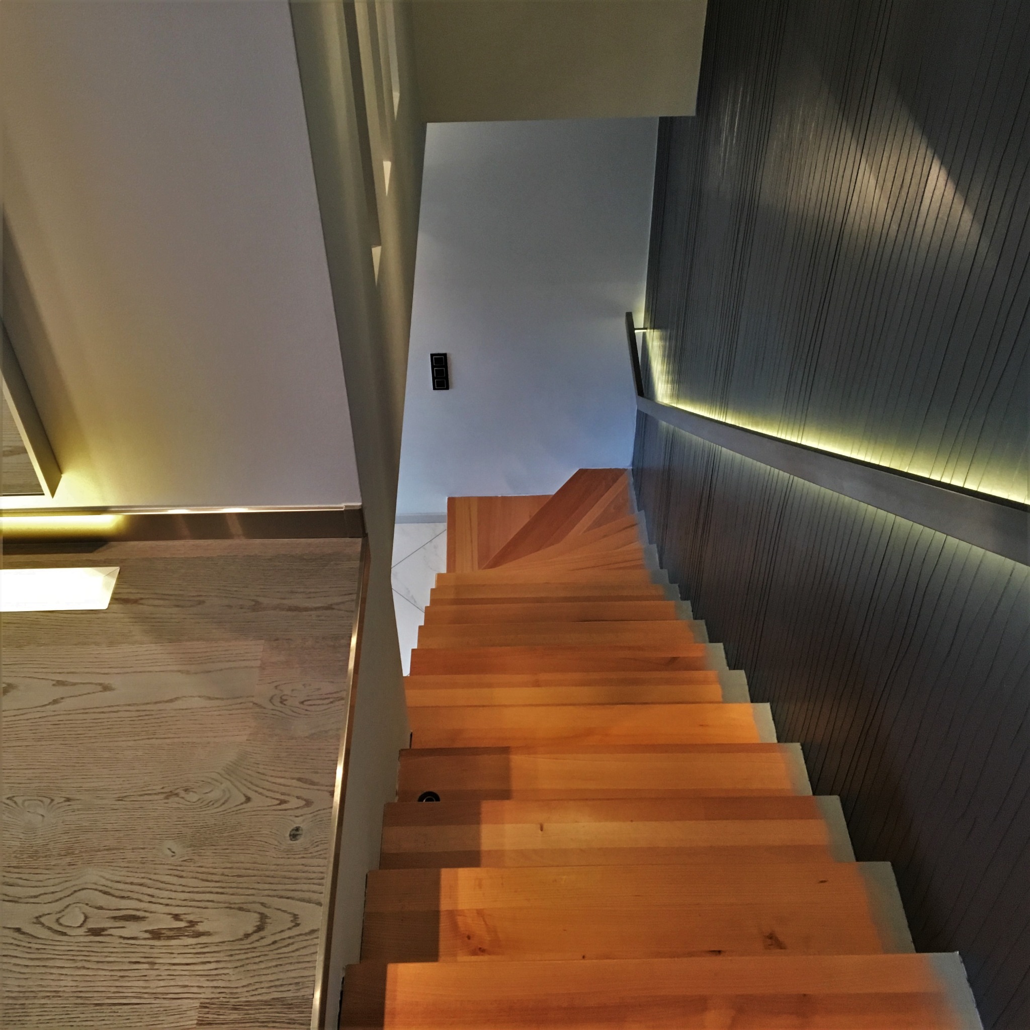 Nowoczesne drewniane schody z podświetleniem LED na ścianie i pod stopniami, widok z góry.