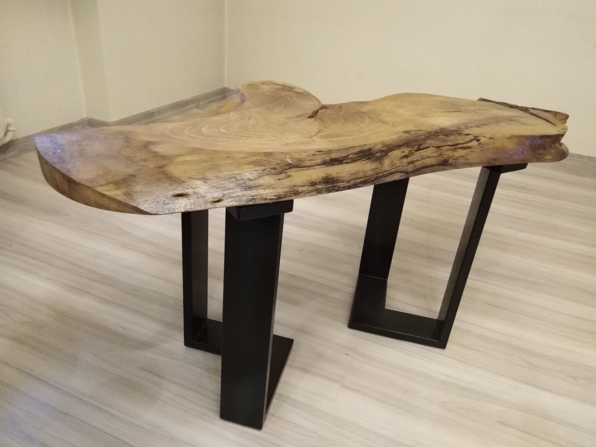 Stolik kawowy z blatem z naturalnego drewna o nieregularnym kształcie i czarnymi, metalowymi nogami w stylu industrialnym.