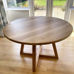 Karol Wincenciak - Jasny, okrągły stół z drewna dębowego na tle okna z widokiem na ogród. Minimalistyczny design, naturalne światło, drewniana podłoga.