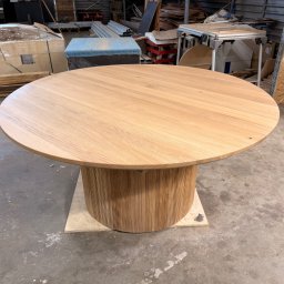 Karol Wincenciak - Okrągły stół z jasnego drewna z cylindryczną podstawą z listewek, stojący na betonowej podłodze w warsztacie, z widocznymi narzędziami i materiałami w tle.