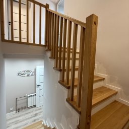 Karol Wincenciak - Jasne, drewniane schody z balustradą w nowoczesnym domu. Widoczne niedoskonałości wykończenia, podkreślające ręczny charakter pracy. Ujęcie z dołu, w kierunku góry.