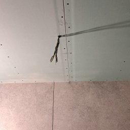 Tar-Bud - Niedokończony sufit z płyt gipsowo-kartonowych z wystającymi przewodami elektrycznymi, widoczne ślady po wkrętach i numer '1328' napisany ołówkiem, dolna część kadru pokazuje fragment ściany...