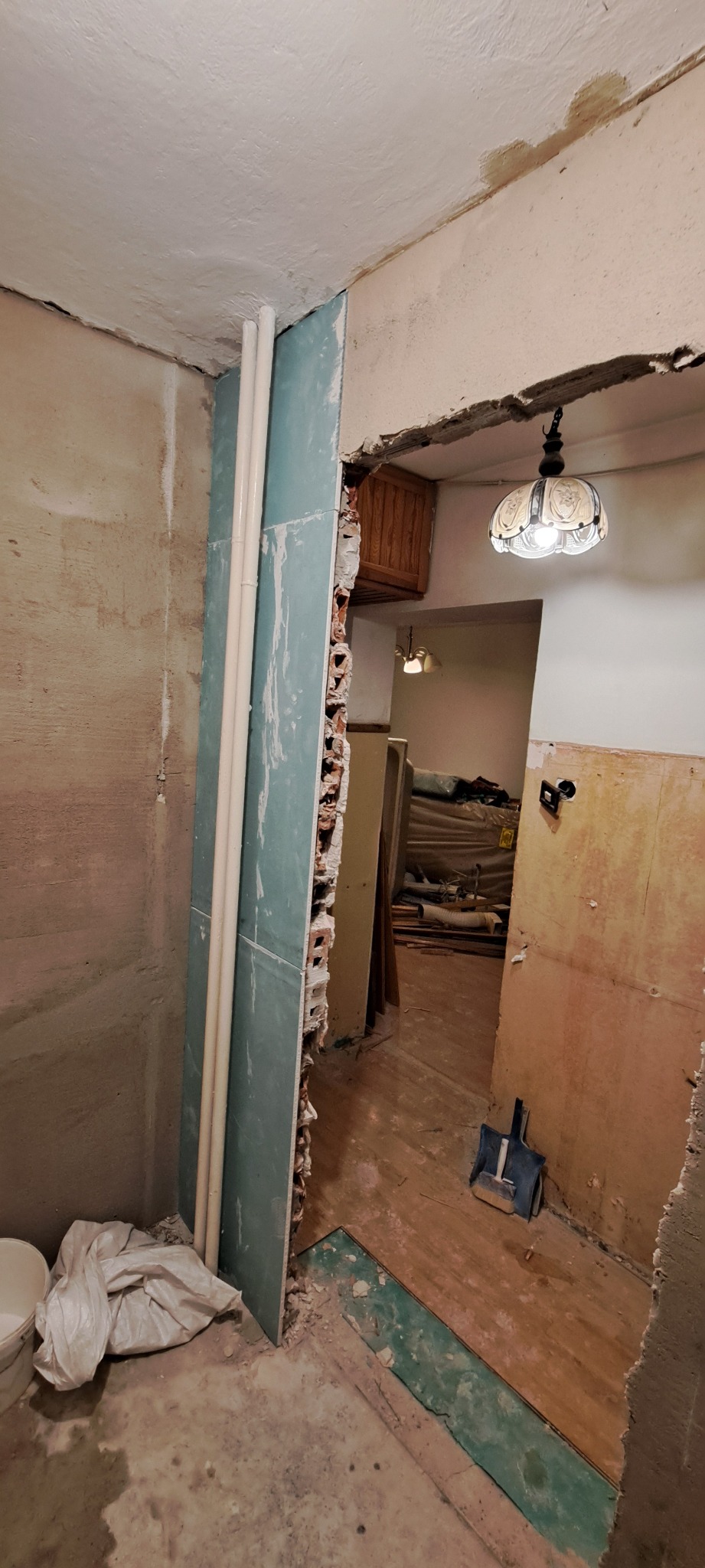 Demontaż ściany działowej w trakcie remontu, widoczne odsłonięte cegły, instalacja wodna i fragment podłogi z resztkami materiałów budowlanych.