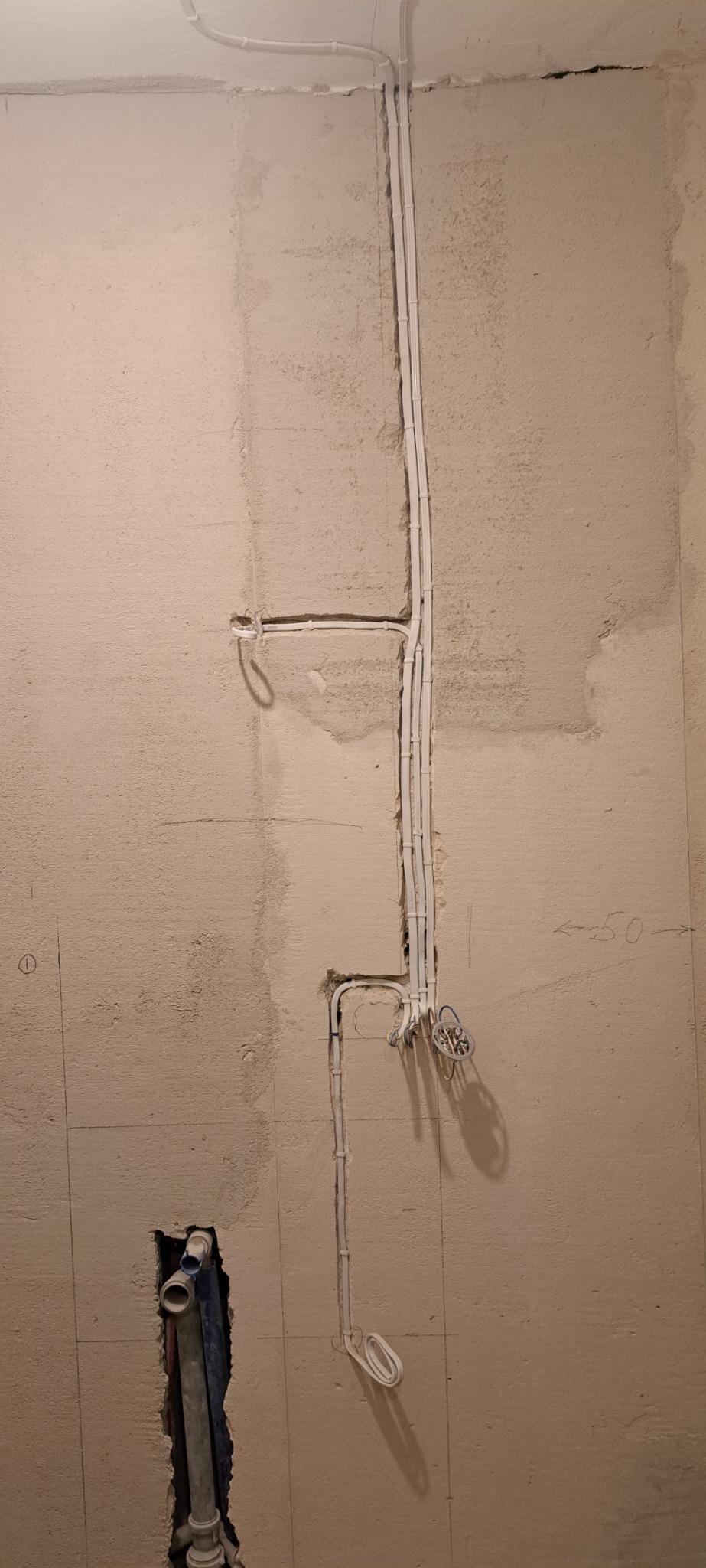 Ściana w trakcie prac instalacyjnych: widoczne przewody elektryczne w peszlach oraz rury kanalizacyjne w wykuciu.