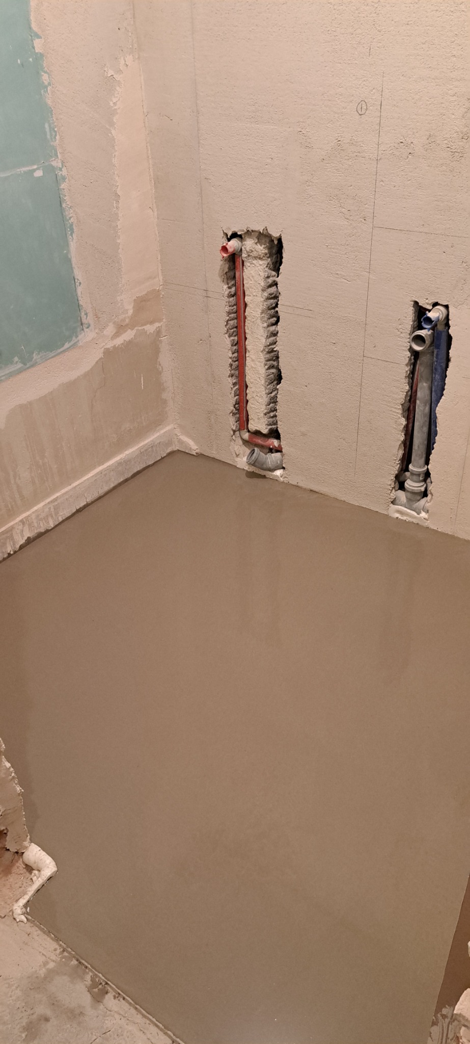 Wylewka podłogowa w łazience, widoczne przygotowane otwory na instalacje wodno-kanalizacyjne w ścianie z surowym tynkiem.