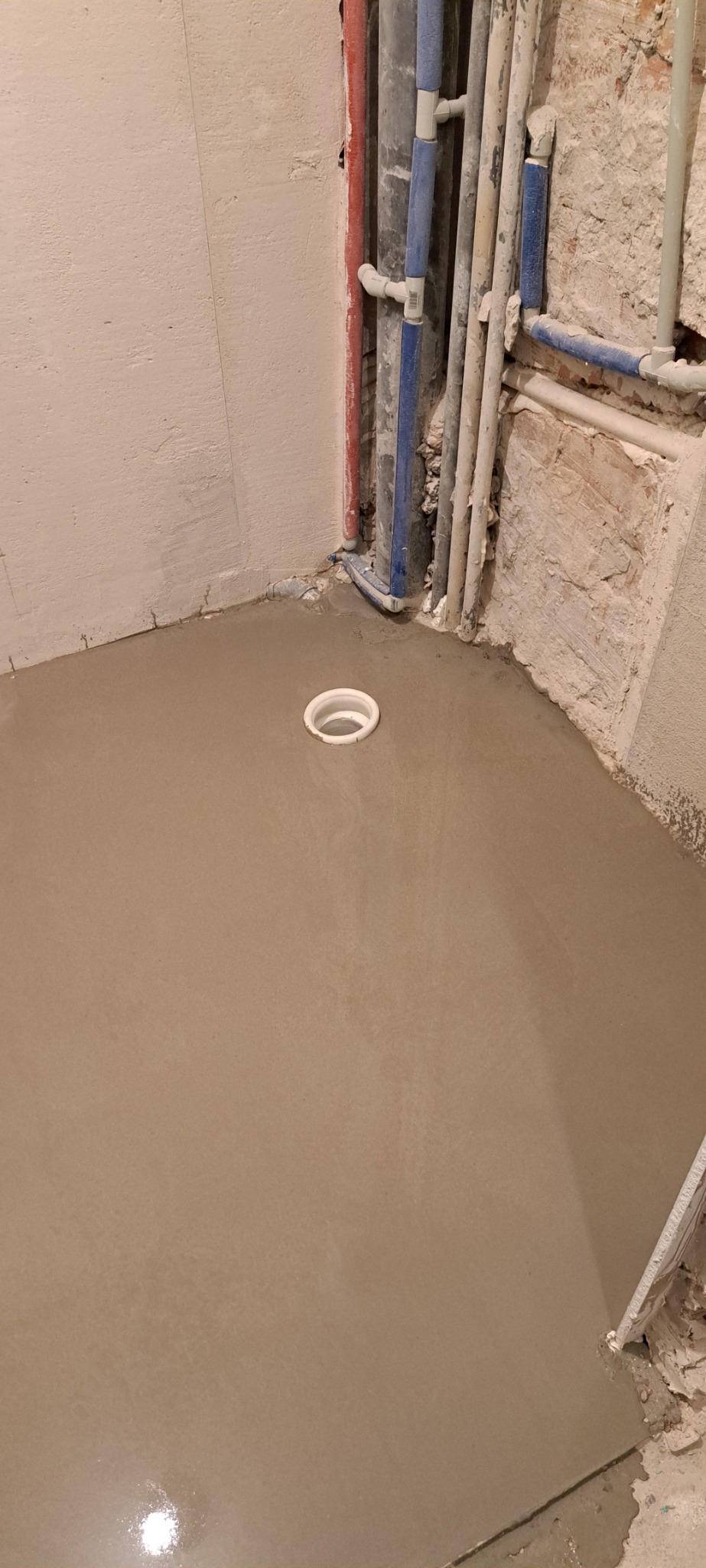 Wylewka samopoziomująca w łazience w trakcie prac, widoczne rury doprowadzające wodę i odpływ podłogowy.