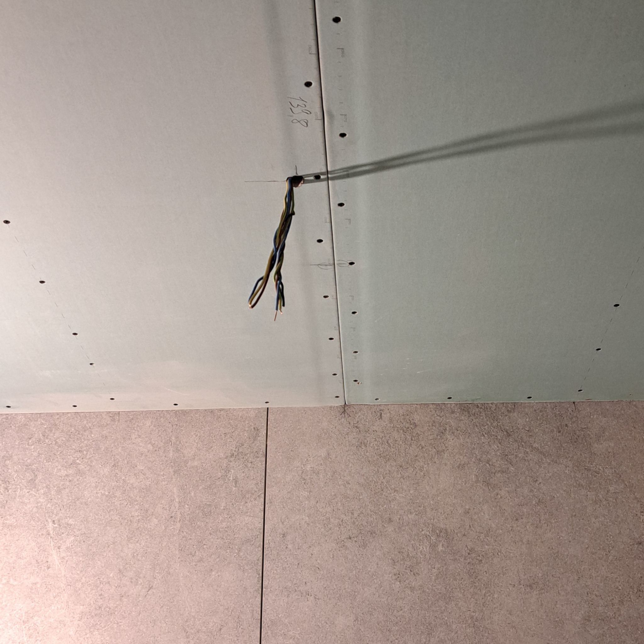 Niedokończony sufit z płyt gipsowo-kartonowych z wystającymi przewodami elektrycznymi, widoczne ślady po wkrętach i numer '1328' napisany ołówkiem, dolna część kadru pokazuje fragment ściany...