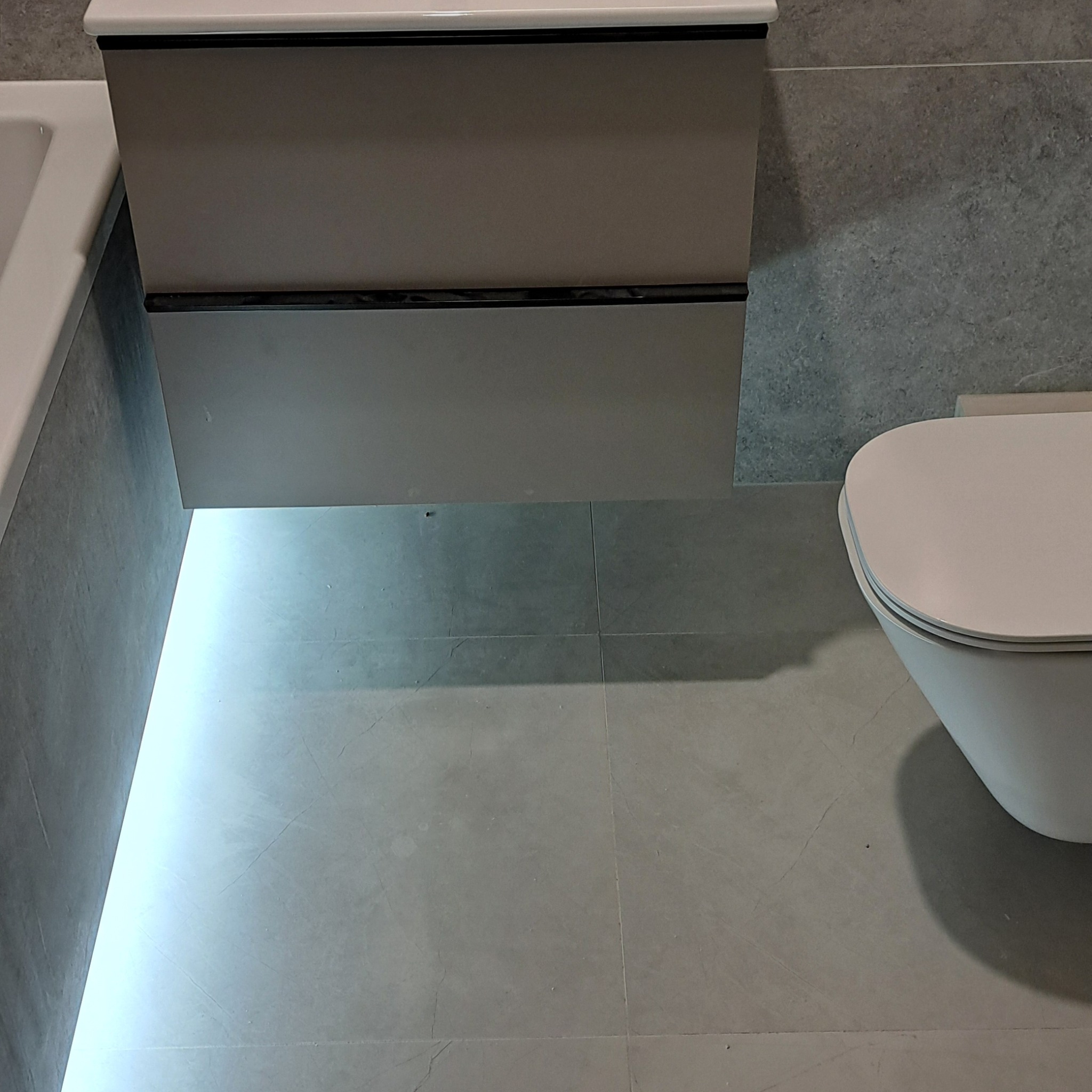 Nowoczesna łazienka z podświetlaną szafką pod umywalką i wiszącą toaletą, szare płytki podłogowe i ścienne.