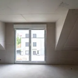 Poddasze w trakcie wykańczania z płyt kartonowo-gipsowych, widoczne łączenia płyt i szkic instalacji na suficie, okno z roletami w tle.