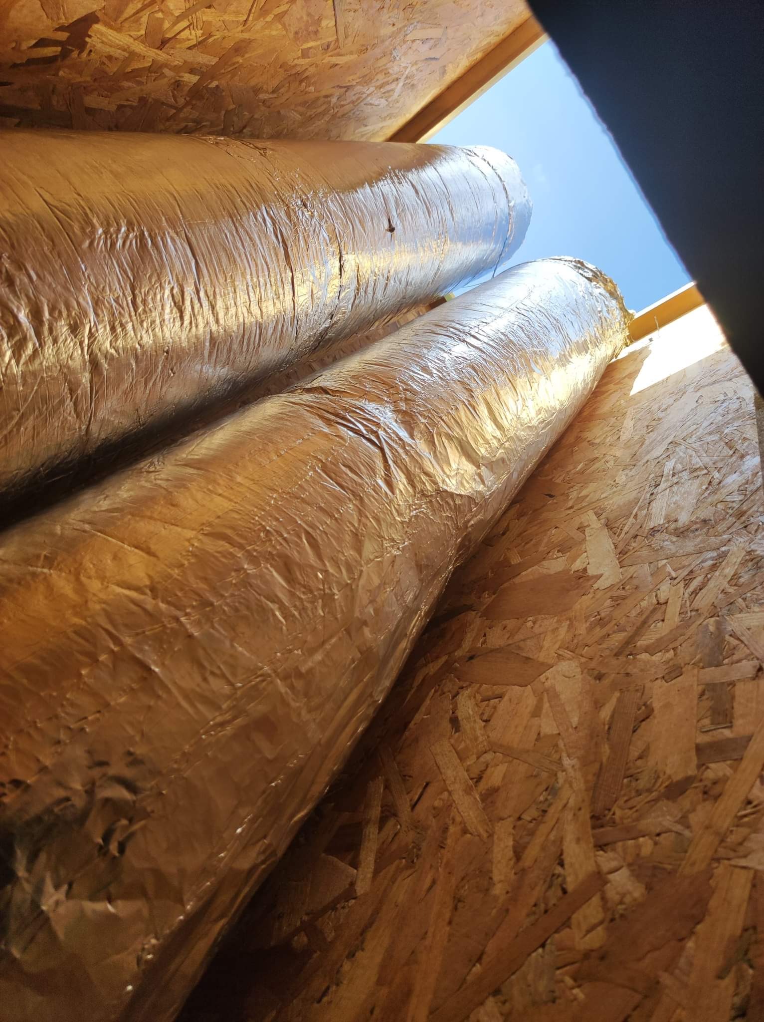 Dwa zaizolowane przewody wentylacyjne z widocznym fragmentem błękitnego nieba przez otwór w suficie, instalacja w Gdańsku.