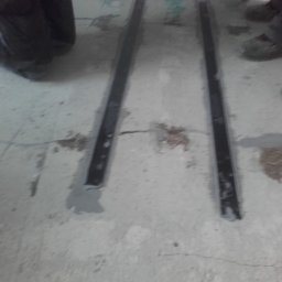 Usługi Budowlane - Inwestycyjne - Przygotowanie podłoża pod posadzkę: widoczne listwy dylatacyjne i zalane szpary w betonie, fragmenty obuwia roboczego w tle.