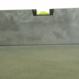 Poziomica na świeżo wylanej, szarej posadzce, sprawdzająca równość powierzchni.