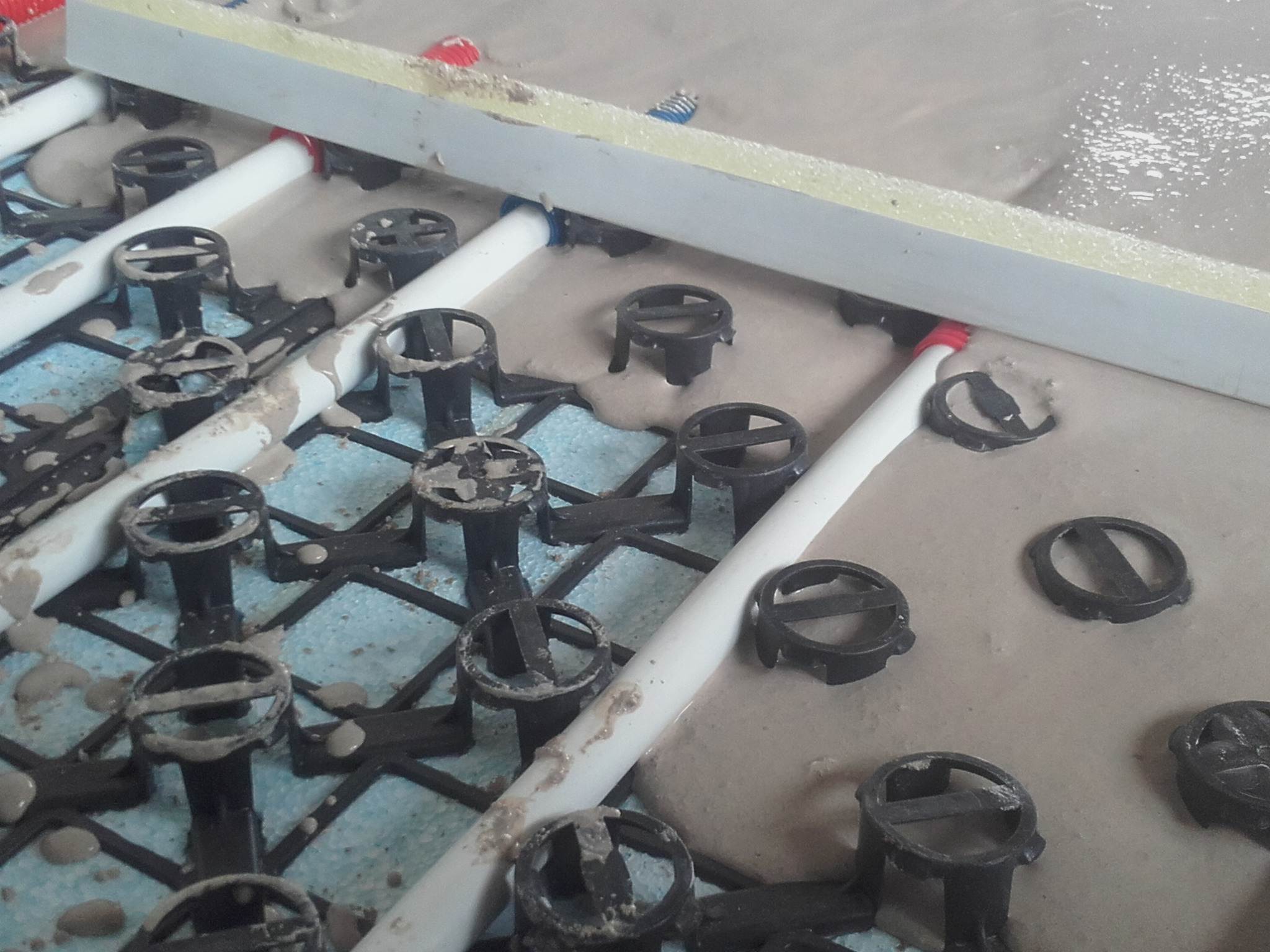 Wylewka anhydrytowa w trakcie rozprowadzania, widoczne rury ogrzewania podłogowego, elementy montażowe i listwa wyrównująca.