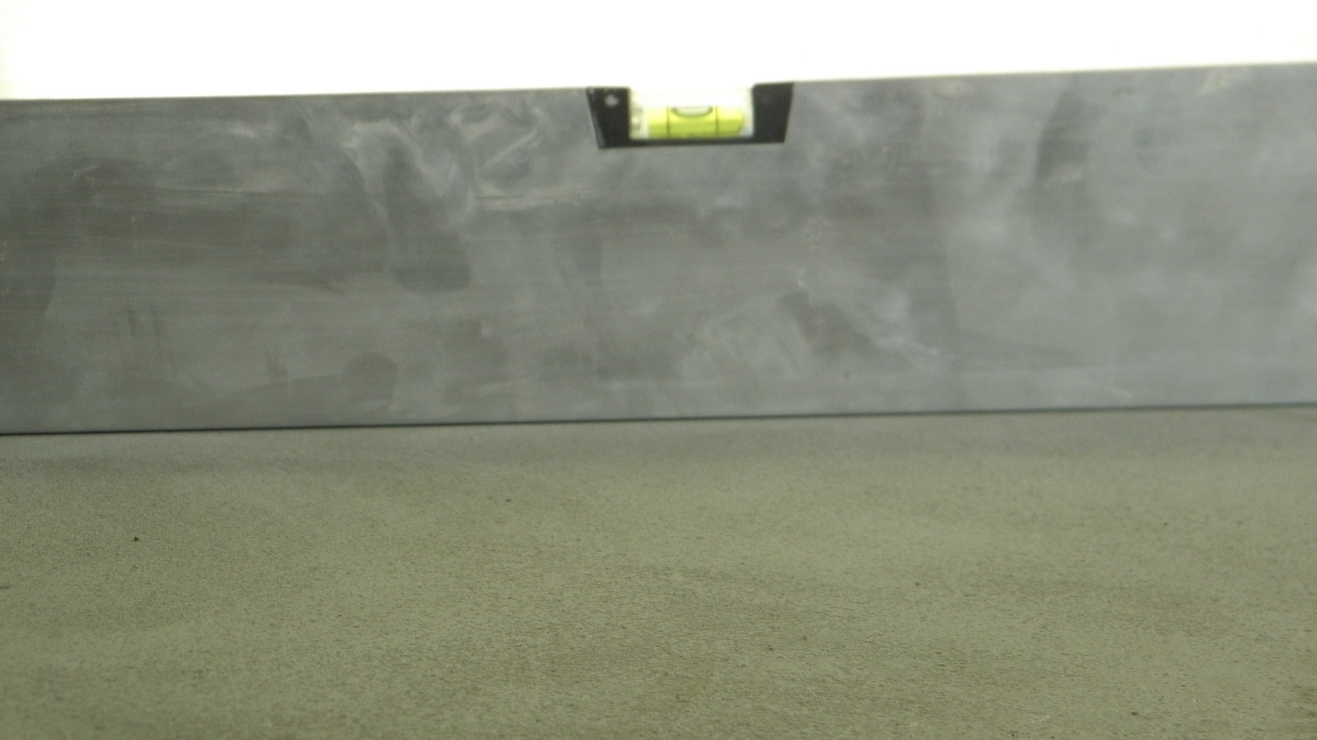 Poziomica na świeżo wylanej, szarej posadzce, sprawdzająca równość powierzchni.