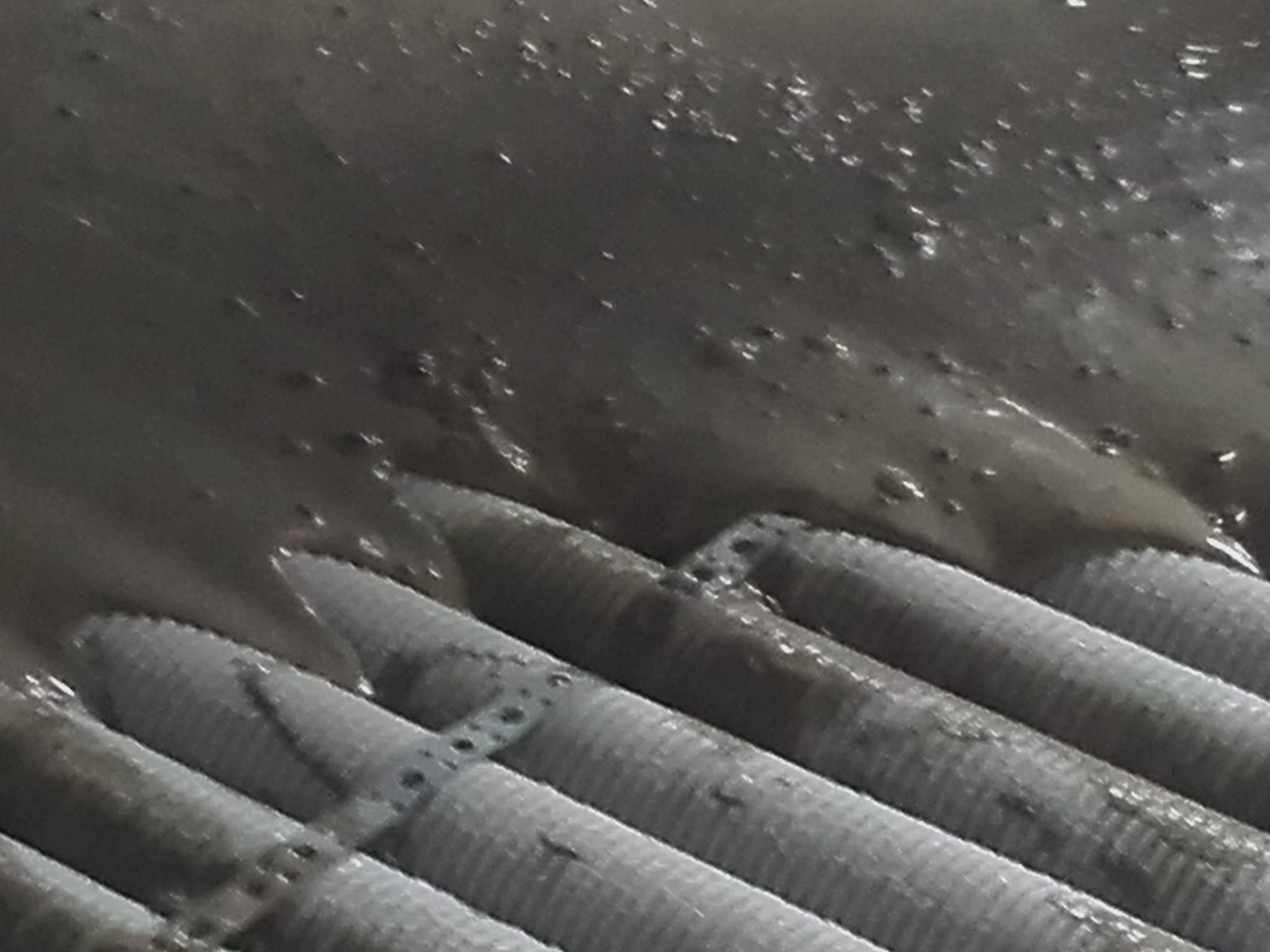 Świeżo wylana, mokra powierzchnia posadzki z widocznymi elementami grzewczymi w podłodze, pokryta błyszczącą warstwą w ciemnym odcieniu.