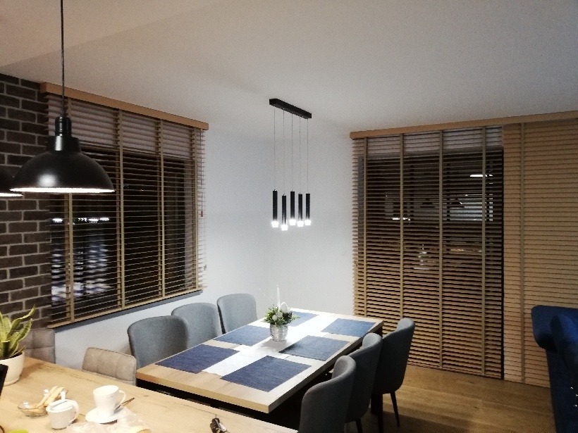 Jadalnia z drewnianymi żaluzjami poziomymi, szarymi krzesłami i nowoczesną lampą wiszącą nad stołem.