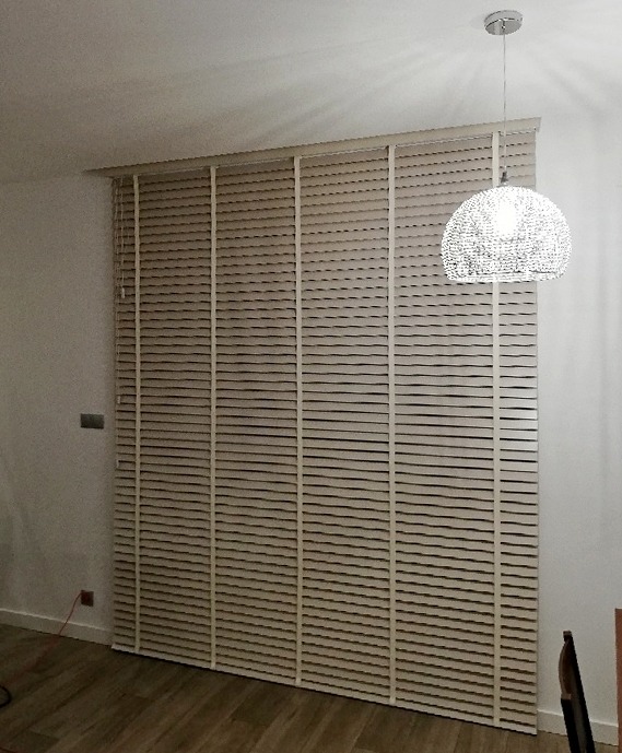 Zasłonięte okno z drewnianymi żaluzjami w kolorze jasnego drewna, z widoczną ozdobną lampą sufitową o kulistym kształcie.