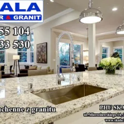 Kuchnia z blatem o wzorze granitowym, z widocznym zlewem i baterią oraz kwiatami w wazonie na wyspie kuchennej, oświetlona wiszącymi lampami.