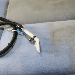 Dysza czyszcząca na tle częściowo wyczyszczonej, jasnoniebieskiej kanapy z widocznym efektem odświeżenia koloru i usuniętych zabrudzeń.