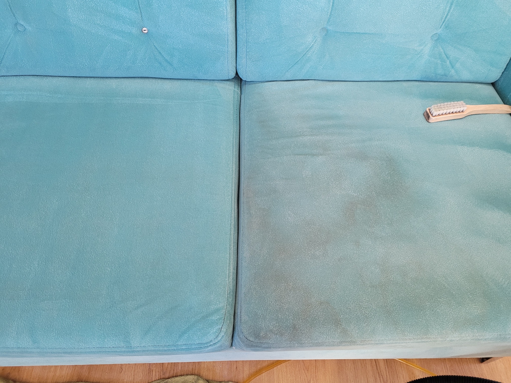 Turkusowa kanapa z widoczną różnicą przed i po czyszczeniu; po prawej stronie widoczna szczotka do tapicerki.