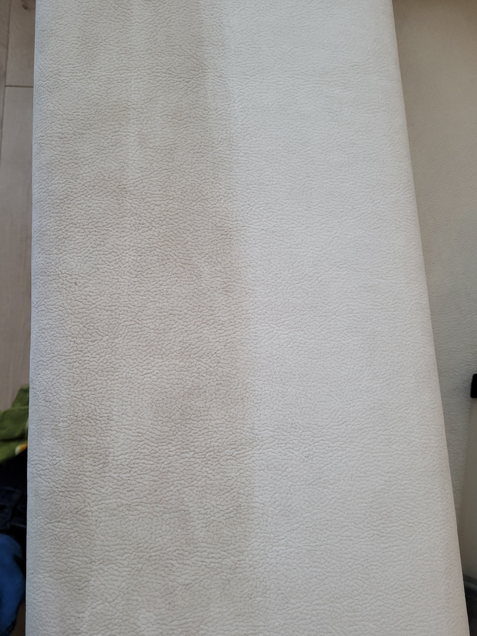 Połowa powierzchni jasnej, tapicerowanej kanapy po czyszczeniu, widoczna wyraźna różnica w odcieniu i czystości.