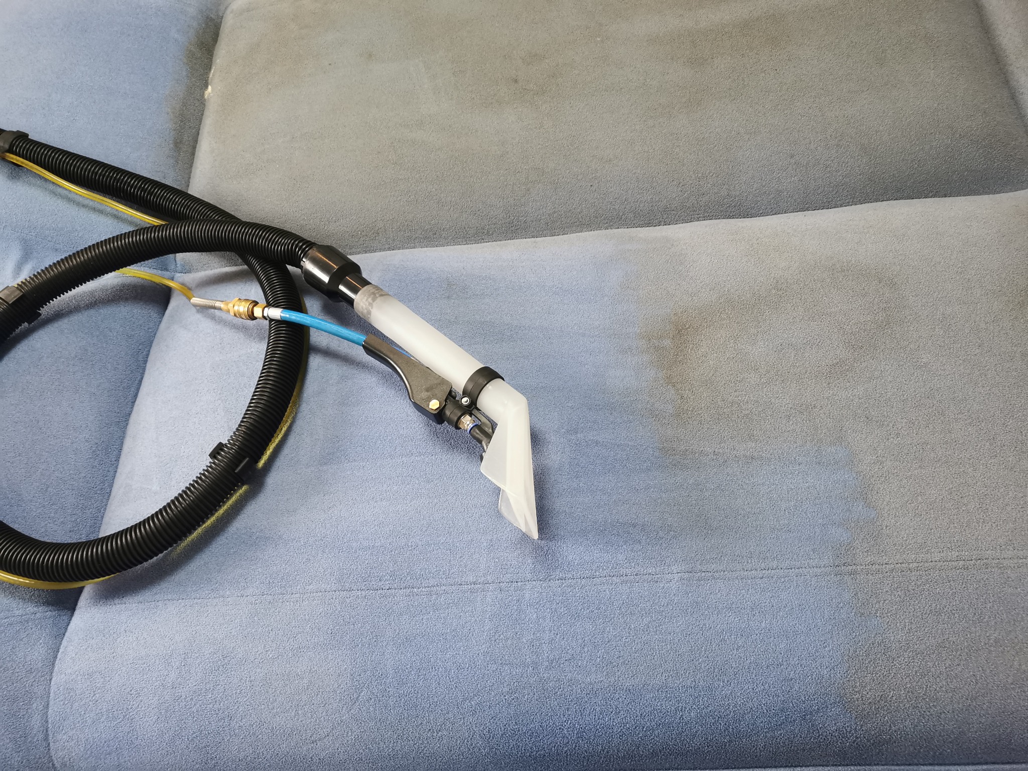 Dysza czyszcząca na tle częściowo wyczyszczonej, jasnoniebieskiej kanapy z widocznym efektem odświeżenia koloru i usuniętych zabrudzeń.