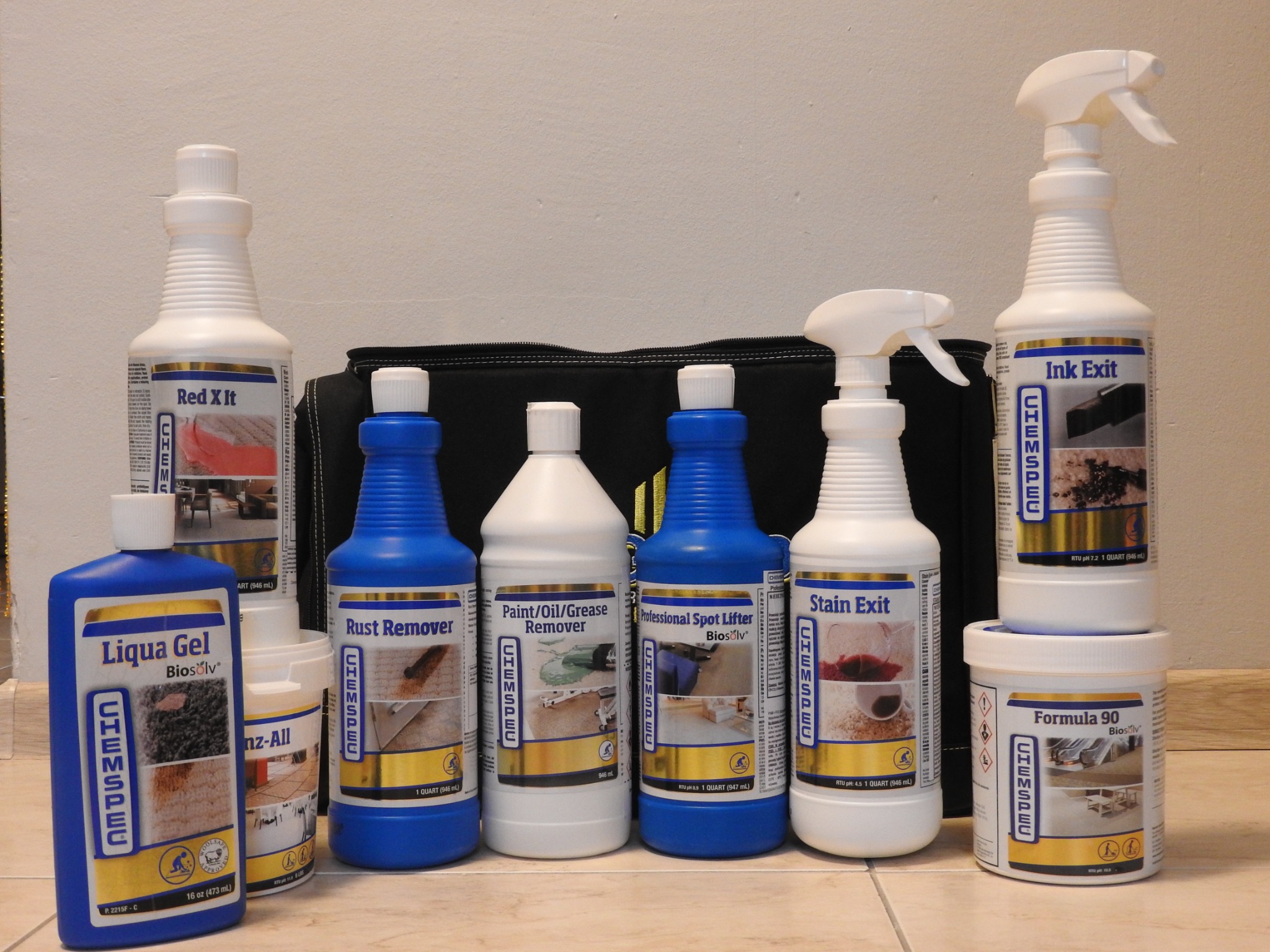 Różnorodne butelki i pojemniki środków czyszczących marki Chemspec, przeznaczone do usuwania plam z dywanów, tapicerek i innych powierzchni, ustawione rzędem na podłodze.