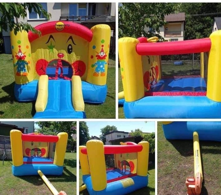 Kolorowy, dmuchany zamek z motywem klauna i zjeżdżalnią, rozłożony na trawniku przed domem.