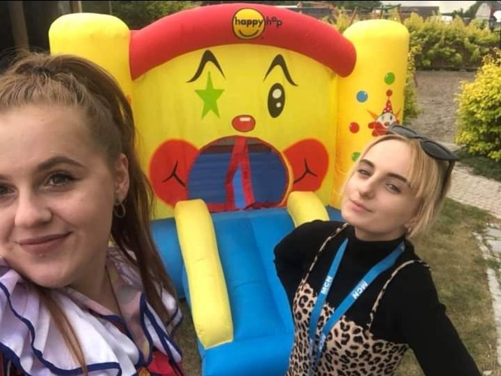 Dwie młode kobiety pozują na tle dmuchanego zamku w Lublinie, zamek ma motyw klauna i zjeżdżalnię.