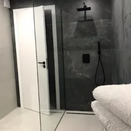 Nowoczesna łazienka z kabiną prysznicową typu walk-in, szare płytki imitujące marmur, czarna armatura, białe drzwi i podświetlana podłoga.