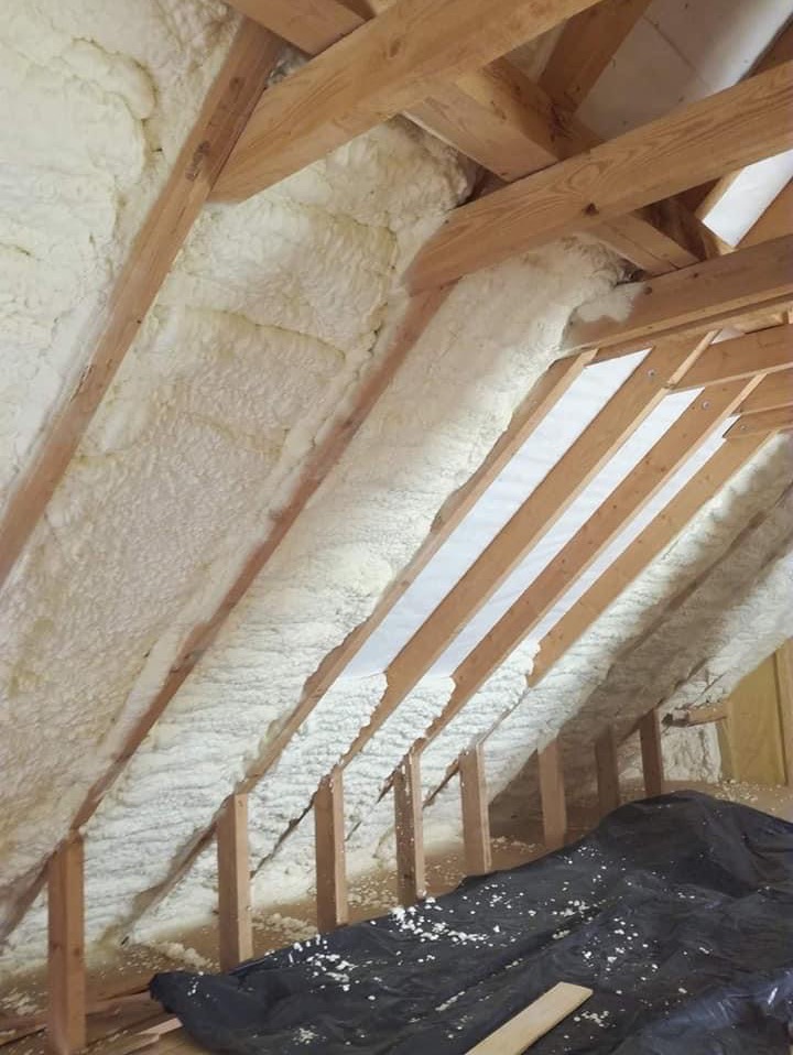 Poddasze z drewnianą konstrukcją krokwiową wypełnione pianką izolacyjną, zabezpieczone folią budowlaną na podłodze.