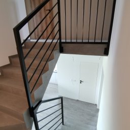 Kraft Design - Wnętrze z betonowymi schodami i czarną, minimalistyczną balustradą z poziomych prętów, widok z góry na dół, z widocznymi elementami wykończenia.