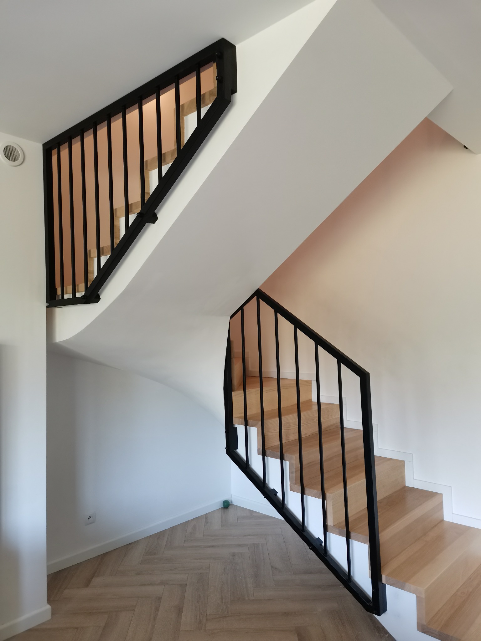 Nowoczesne schody drewniane z czarną, metalową konstrukcją i minimalistyczną balustradą, widok z dołu na jasne wnętrze.